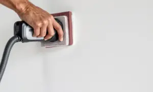 Main tenant utilise un aspirateur pour nettoyer le mur après ponçage.