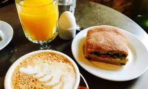 En kopp kaffe med lattekonst, apelsinjuice, ett kokt ägg och en macka. En perfekt frukost som ger en känsla av comfort food.