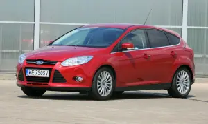 Czerwony Ford Focus z włączonymi światłami mijania, zaparkowany przed nowoczesnym budynkiem.