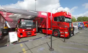 Deux camions de course rouges, prêts pour la vitesse max, sont garés sous une tente. L'un porte le numéro 24.