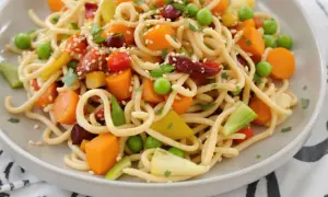 Assiette de nouilles sautées colorées avec carottes, petits pois, poivrons et garniture de sésame. Une recette facile et savoureuse.