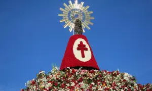 Estatua de la Virgen adornada con flores rojas y blancas, con una cruz en el centro. Un evento de **pilares fiesta** que celebra la fe y la tradición.