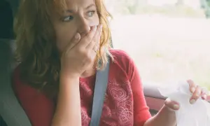 Kobieta w samochodzie zakrywa usta, czując mdłości. Może to być skutek choroby lokomocyjnej, na którą pomaga difenhydramina.