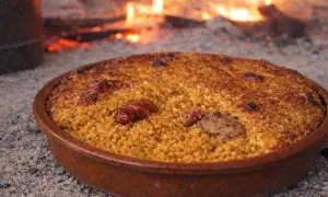 Arroz con costra recién hecho, con trozos de carne y salchicha, cocinándose a la leña.
