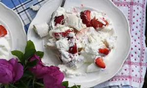 En härlig Eton Mess med färska jordgubbar och marängbitar, serverad på en vit tallrik med en vacker duk och rosor.