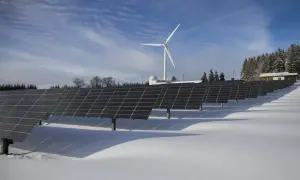 Panele słoneczne i wiatrak na ośnieżonym polu. W tle las i budynek. Taka instalacja może pomóc w stabilizacji opłata sieciowa zmienna całodobowa.