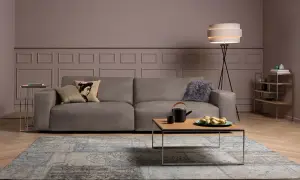 Gemütliches Wohnzimmer mit einem Sofa in Farbe Taupe, einem Couchtisch mit Teekanne und Früchten, sowie einem Teppich.