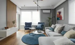 Jasny salon z dwoma oknami na jednej ścianie, niebieskimi fotelami i sofą.