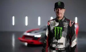 Ken Block, piloto de rally, posa con su traje de competición y un coche de Audi e-tron detrás.