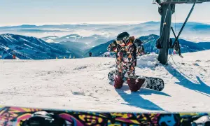 Dziecko w kolorowym kombinezonie przygotowuje się do zjazdu na snowboardzie. Idealne miejsce, gdzie na narty w Czechach z dziećmi.