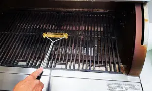 En hand rengör gallret på en gasolgrill under tak med en grillborste.