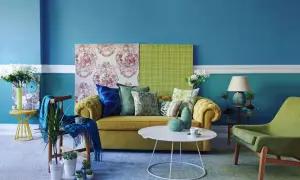 Soggiorno con divano giallo, cuscini verdi e blu, e pareti blu. Ottime idee per colorare le pareti di casa con contrasti vivaci.