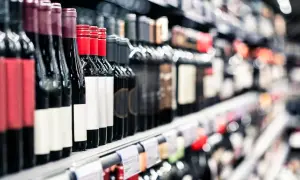 Rzędy butelek wina na półce sklepowej. Widać etykiety i ceny alkoholu, zachęcające do wyboru.