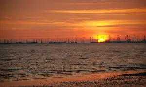 Sonnenuntergang am Emden Strand mit Windrädern und glitzerndem Wasser.