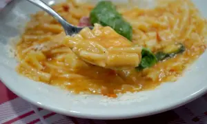 Un cucchiaio di pasta con patate cremosa, condita con basilico fresco e parmigiano grattugiato.
