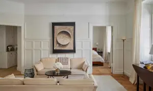 Vardagsrum med beigefärgad soffa, konstverk och en öppen dörr till sovrum. En vacker renovering av ett sekelskifteshus.