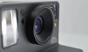 Zbliżenie na obiektyw aparatu Polaroid One Step 2. Widoczny błysk flesza i detale obudowy, sugerujące eksperymenty z bracketingiem ostrości.