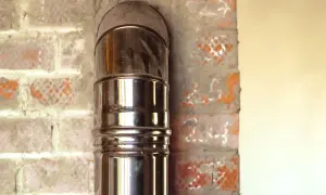 Błyszcząca rura kominowa, element podłączenia pieca na pellet, wychodzi z ceglanej ściany.