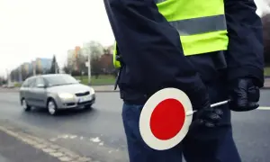 Agent de police en uniforme, gilet fluorescent, tenant un panneau stop. Contrôle routier, papier obligatoire.