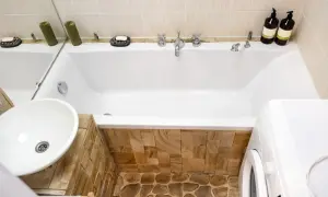 Badezimmer mit Waschbecken, Badewanne verkleiden mit Naturstein und Waschmaschine.