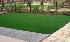 Césped artificial verde vibrante junto a una terraza de madera gris. El césped artificial puede generar electricidad estática.