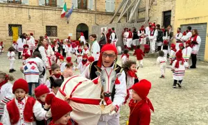 Un uomo con un costume da toro guida una sfilata di bambini vestiti di rosso e bianco per il carnevale nelle Marche.