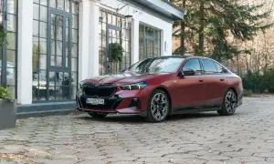 Elegancki, bordowy BMW 550e na brukowanym podjeździe przed nowoczesnym budynkiem.