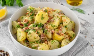 Pyszna sałatka ziemniaczana niemiecka z boczkiem i ziołami, podana w białej misce.
