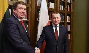 Dwóch polityków ściska sobie dłonie na tle flag Polski i Litwy.