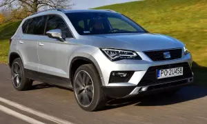 Srebrny Seat Ateca w ruchu. Kierowca za kierownicą, zielone wzgórza w tle. Wiele osób szuka seat ateca opinie przed zakupem.