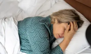 Een vrouw ligt in bed, met haar hand op haar voorhoofd. Ze vraagt zich af: waarom voel ik me zo moe?