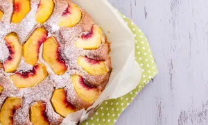 Saftiger Pfirsichkuchen, mit Puderzucker bestäubt, auf einem grünen Tupftuch. Ein Genuss für die Sinne!