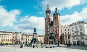 Rynek Główny w Krakowie z Kościołem Mariackim i pomnikiem Mickiewicza. Stare miasto Kraków tętni życiem pod błękitnym niebem.