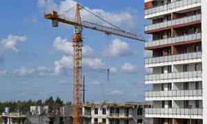 Plac budowy z dźwigiem i budynkami mieszkalnymi w tle.