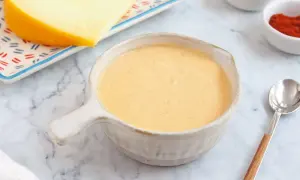 Crema de salsa de queso lista para servir, con un trozo de queso y especias al fondo.
