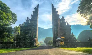 Brama na Bali, porośnięta mchem, zaprasza do podróży. Słońce wschodzi nad górami, a mgła otula krajobraz.