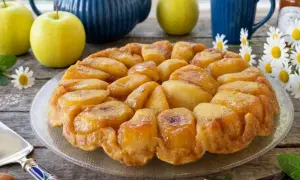 Una deliziosa tarte tatin di mele dorate, con mele fresche, una teiera blu e fiori di campo.