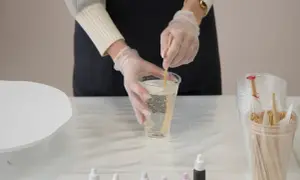 Mani guantate mescolano resina epossidica in un bicchiere, un passo fondamentale per imparare come usare la resina epossidica sul legno per creare opere d'arte uniche.