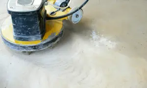 Maschine schleift Beton. Staub wirbelt auf, während die rotierende Scheibe den Boden glättet.