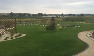 Zadbany ogród z trawnikiem, kamiennymi ścieżkami i rabatami. W tle jezioro i pola. Fosforan monopotasowy pomógł uzyskać tak piękny, zielony trawnik.