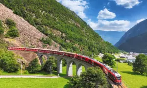 Czerwony pociąg Bernina Express na kamiennym wiadukcie, malownicza trasa i ceny podróży przez Alpy.