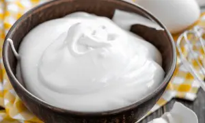 Perfekt geschlagener Eischnee in einer Schüssel, bereit für süße Kreationen. Daneben liegen Eier und ein Schneebesen.