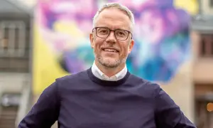 Niclas Hermansson ler glatt framför en färgglad väggmålning.