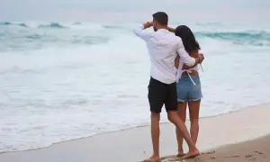 Ett par njuter av sin semester i Danmark vid havet. Mannen spanar ut mot vågorna medan kvinnan kramar om honom.