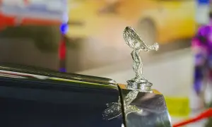 Den ikoniska Rolls-Royce kylarprydnad, "Spirit of Ecstasy", glänser på en mörk bil.