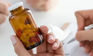 Dłoń trzyma brązowy **ranozek** z żółtymi i czerwonymi tabletkami. W tle ktoś pisze.