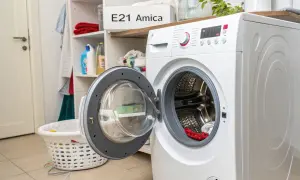 Pralka Amica z otwartymi drzwiczkami, na półce widoczny napis "E21 Amica", sugerujący błąd. Obok kosz na pranie.