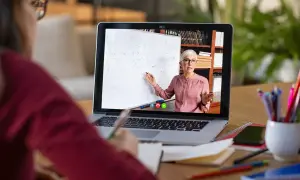 Nauczycielka prowadzi lekcję online na laptopie, wskazując na tablicę z równaniami.
