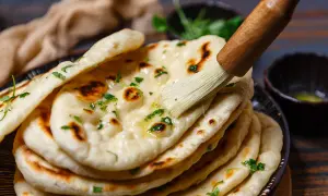 Frisch gebackenes indisches Fladenbrot wird mit Butter bestrichen und mit Koriander bestreut.