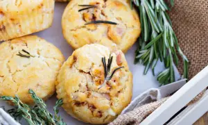 Vier herzhafte Muffins mit Rosmarin und Speck, garniert mit frischen Kräutern, liegen in einer Holzkiste.
